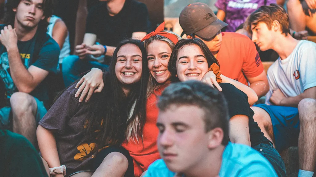 A group of young adults celebrate outside as three women hug eachother